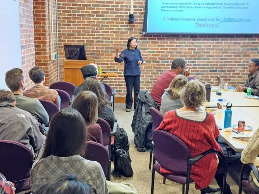 Professor presenting her research, standing in front of room full of faculty and students..